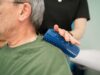 Therapeutin rollt mit der Igelrolle über die Schulter des Patienten